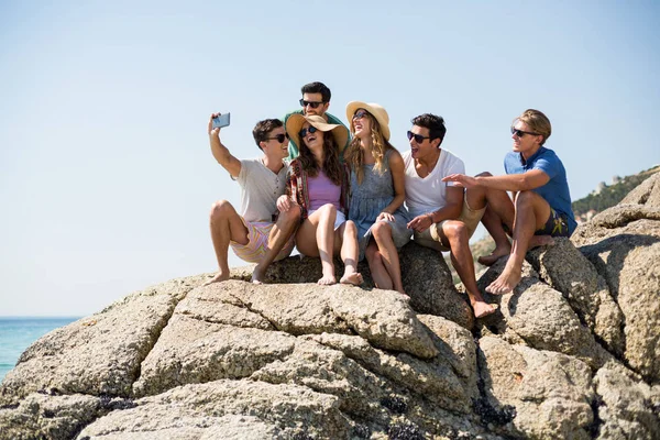 Amigos tomando selfie mientras están sentados en formaciones rocosas — Foto de Stock