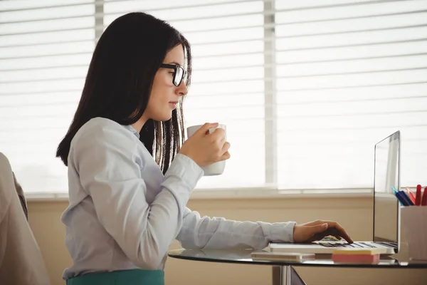 Жінка п'є каву, сидячи за ноутбуком — стокове фото