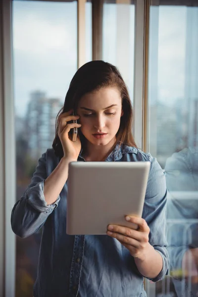 O femeie vorbind pe mobil în timp ce se uită la tabletă — Fotografie, imagine de stoc