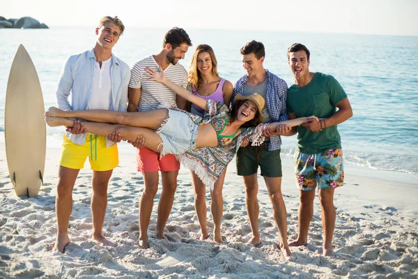Amigos sosteniendo mujer joven en la playa —  Fotos de Stock