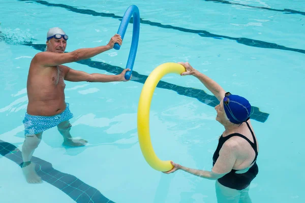 Casal de idosos exercitando com macarrão de piscina — Fotografia de Stock