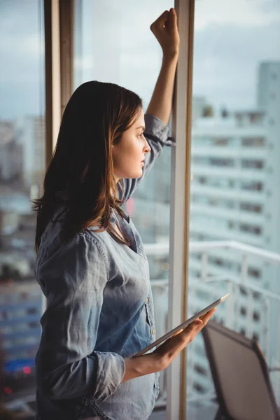 Žena držení tabletu při pohledu přes okno — Stock fotografie