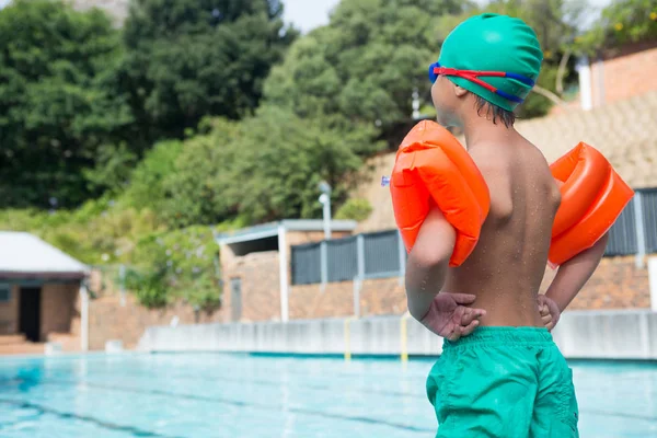 Niño usando brazalete de pie junto a la piscina — Foto de Stock