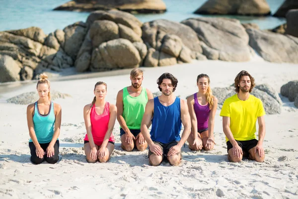 Amigos meditando mientras se arrodillan en la orilla — Foto de Stock