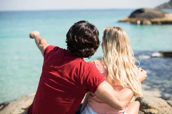 Hombre apuntando hacia el mar mientras está sentado con la mujer — Foto de Stock