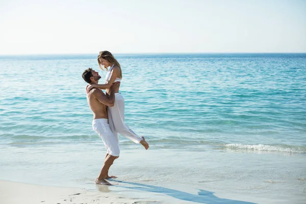 Homem carregando namorada enquanto em pé na praia — Fotografia de Stock