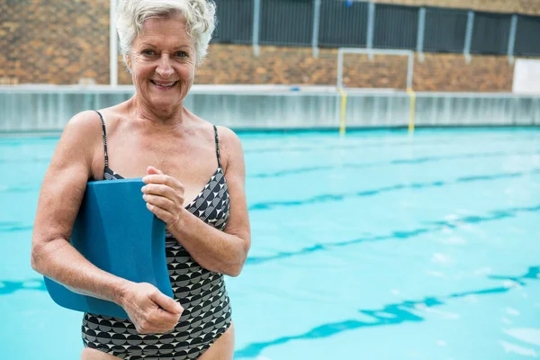 Senior woman holding kickboard at poolside — Stock Photo, Image