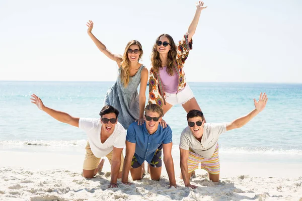 Vänner bildar pyramid med armar upp vid stranden — Stockfoto