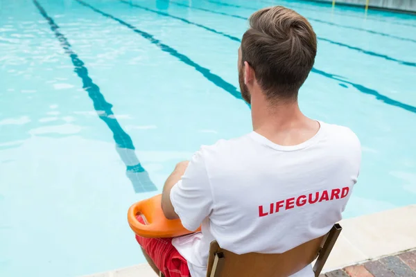 Salva-vidas sentado na cadeira com bóia de resgate à beira da piscina — Fotografia de Stock