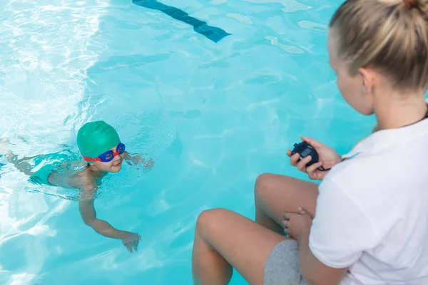 Entrenadora femenina tiempo de seguimiento del niño en la piscina — Foto de Stock