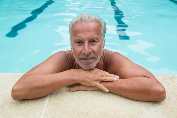 Senior homem inclinado na beira da piscina — Fotografia de Stock