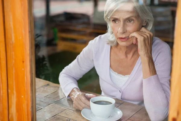 Mujer mayor pensativa sentada junto a la mesa — Foto de Stock