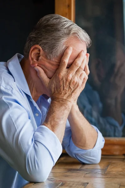 Senior manbeläggning ansikte medan vid bord — Stockfoto