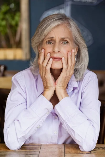 Беспокойная старшая женщина сидит за столом — стоковое фото