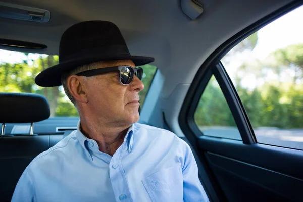 Uomo anziano con occhiali da sole e cappello in auto — Foto Stock