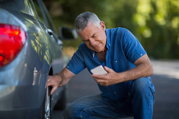 Man met behulp van de telefoon terwijl het controleren van de wielen van de auto — Stockfoto