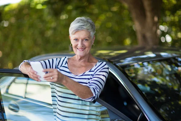 Mujer sosteniendo el teléfono apoyado en la puerta del coche — Foto de Stock