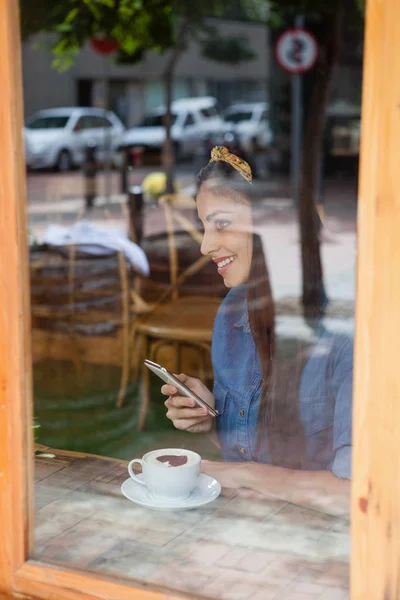 Kvinnan håller telefonen medan du sitter på café — Stockfoto