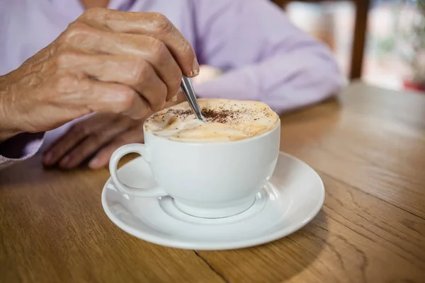 Žena za stálého míchání kávy, zatímco sedí u stolu — Stock fotografie