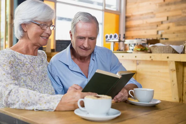 Senior couple reading book while having coffee — Stock Photo, Image