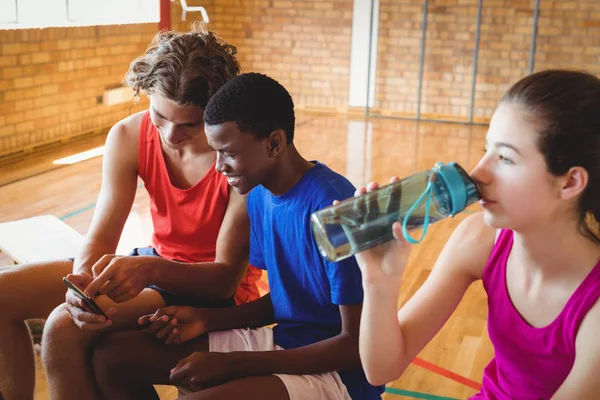 Girl drinking water while boys using phone — Stock Photo, Image