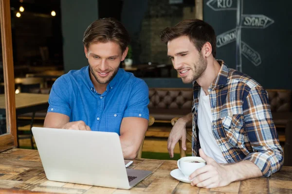 Amigos usando el ordenador portátil mientras están sentados en la mesa — Foto de Stock