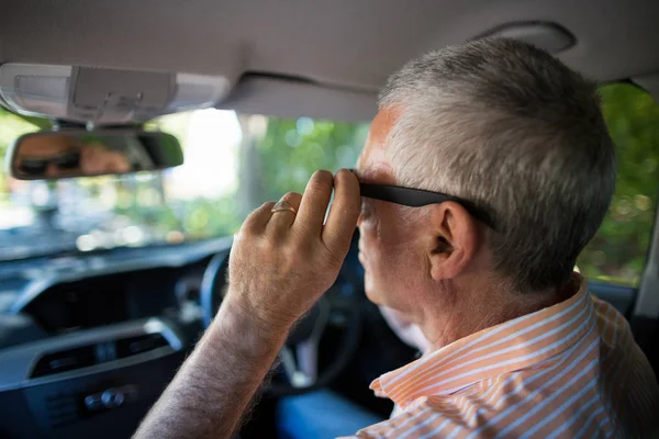 Homem sênior ajustando óculos de sol no carro — Fotografia de Stock