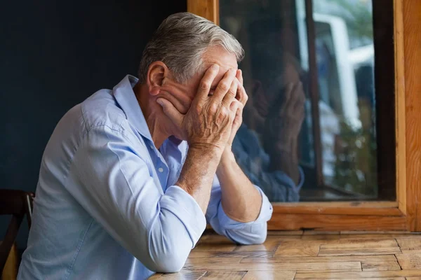 テーブルに座って顔を覆っている年配の男性 — ストック写真