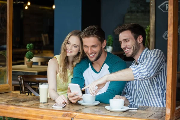 Amigos mirando el teléfono inteligente mientras están sentados junto a la mesa —  Fotos de Stock