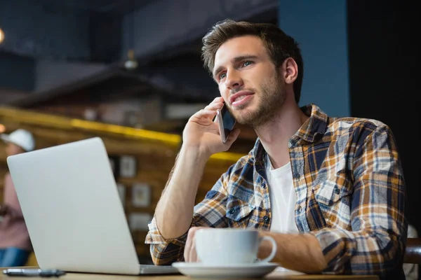 Man talking on phone while using laptop — Stock Photo, Image