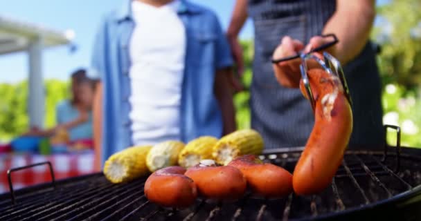 Père et fils grillent saucisses et cors sur barbecue — Video