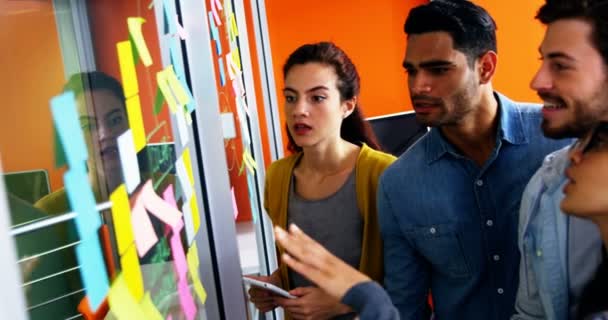 Smiling executives discussing over sticky notes on glass wall — Stock Video