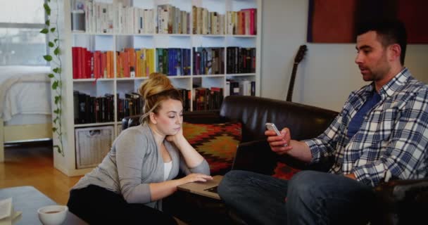 Mujer usando el ordenador portátil mientras que el hombre usando el teléfono móvil en la sala de estar — Vídeos de Stock