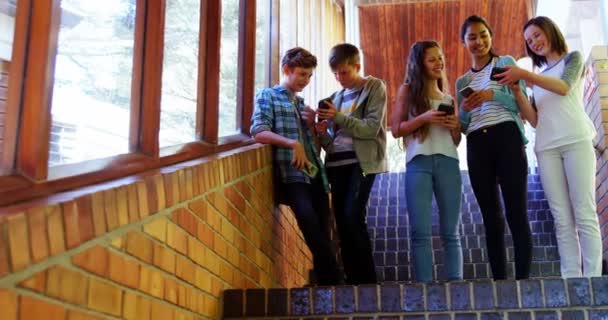 Grupo de amigos sonrientes de la escuela usando el teléfono móvil en el pasillo — Vídeos de Stock