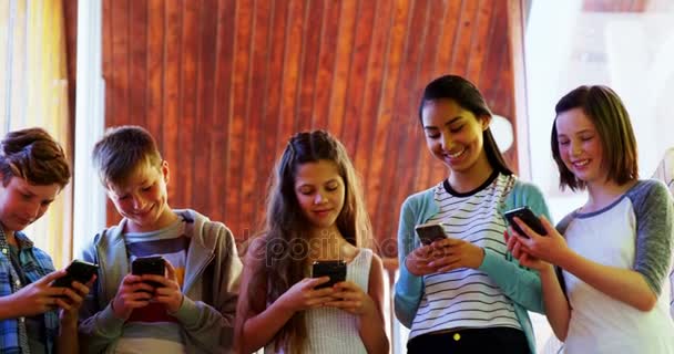 Grupo de amigos sonrientes de la escuela usando el teléfono móvil en el pasillo — Vídeos de Stock