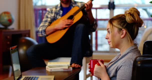 Uomo che suona la chitarra mentre la donna utilizza il computer portatile — Video Stock