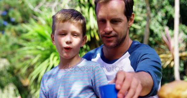 Πατέρα, δίνοντας ένα ποτήρι νερό στο γιο στην του γκαζόν στον κήπο — Αρχείο Βίντεο