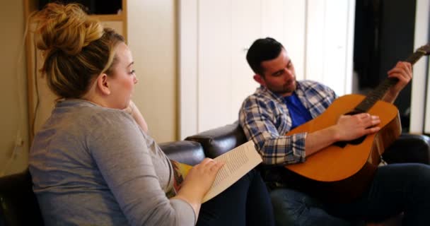 Homem tocando guitarra enquanto mulher lendo livro — Vídeo de Stock