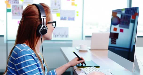 Female graphic designer working while listening music at desk — Stock Video