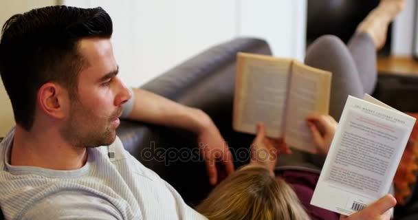 Пара лежащих на диване и читающих книги — стоковое видео
