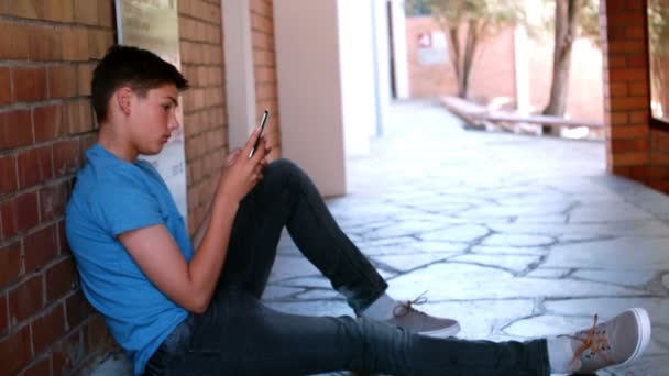 Schoolboy sitting in corridor and using mobile phone — Stock Video