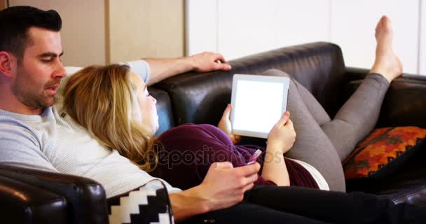 Ζευγάρι χρησιμοποιώντας το κινητό τηλέφωνο και ψηφιακό tablet στον καναπέ — Αρχείο Βίντεο