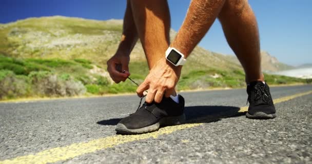 Триатлонист завязывает шнурки на сельской дороге — стоковое видео