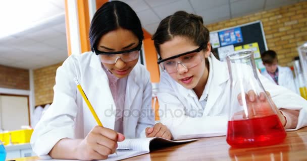 Niñas de la escuela escribiendo en un libro de diario mientras experimentan en laboratorio en la escuela — Vídeos de Stock