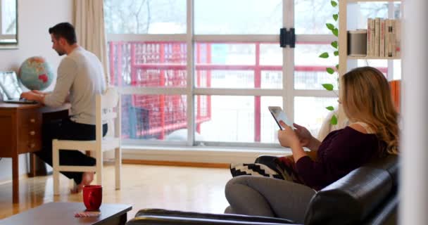 Oturma odasında cep telefonu ve dijital tablet kullanarak çift — Stok video