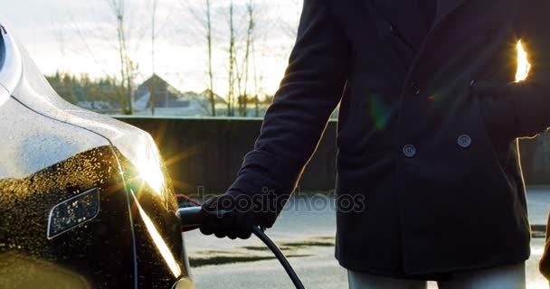 Casal conversando enquanto carrega o carro elétrico em um dia de inverno — Vídeo de Stock