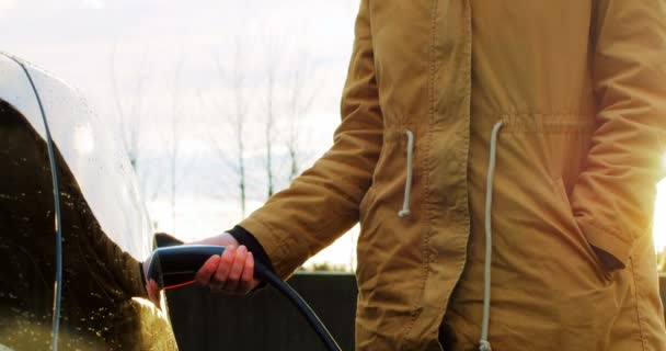 Mujer cargando el coche eléctrico en un día de invierno — Vídeos de Stock