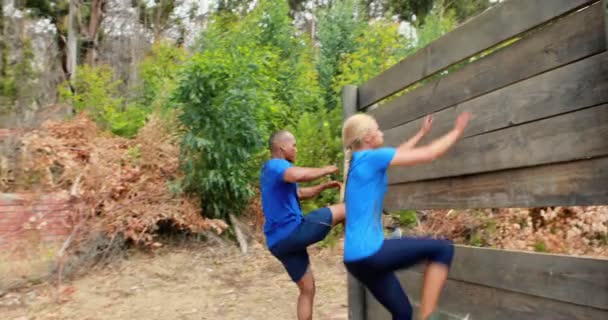 Fit man and woman to climb a wooden wall during obstacle course — Stock Video
