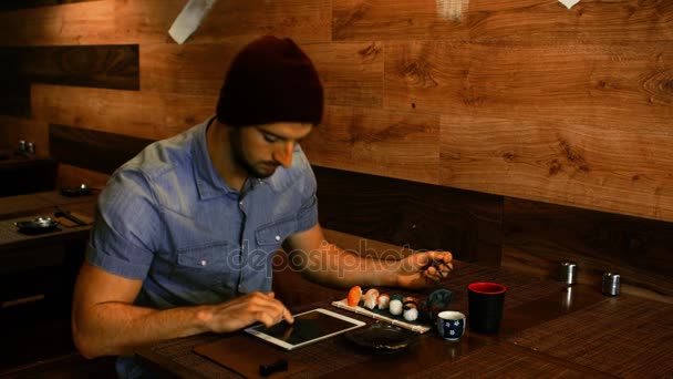 Человек, использующий цифровой планшет во время употребления суши — стоковое видео