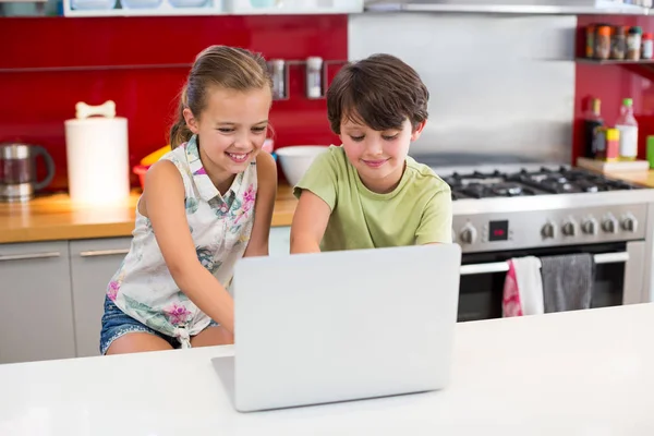 Uśmiechający się rodzeństwo korzysta z laptopa w kuchni — Zdjęcie stockowe